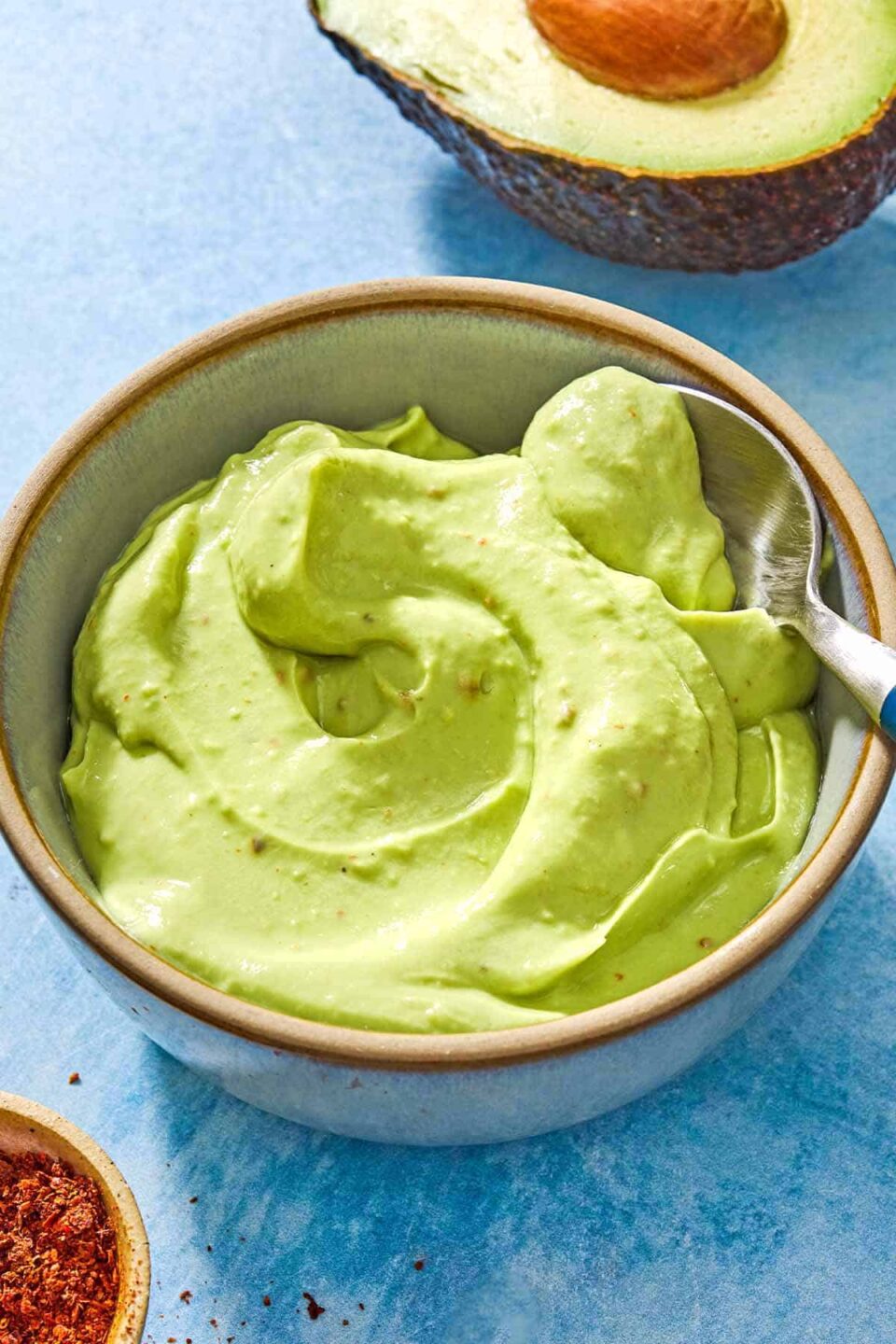 A close up of a stuffed sweet potato with a dollop of avocado crema on a plate with 2 lime wedges.