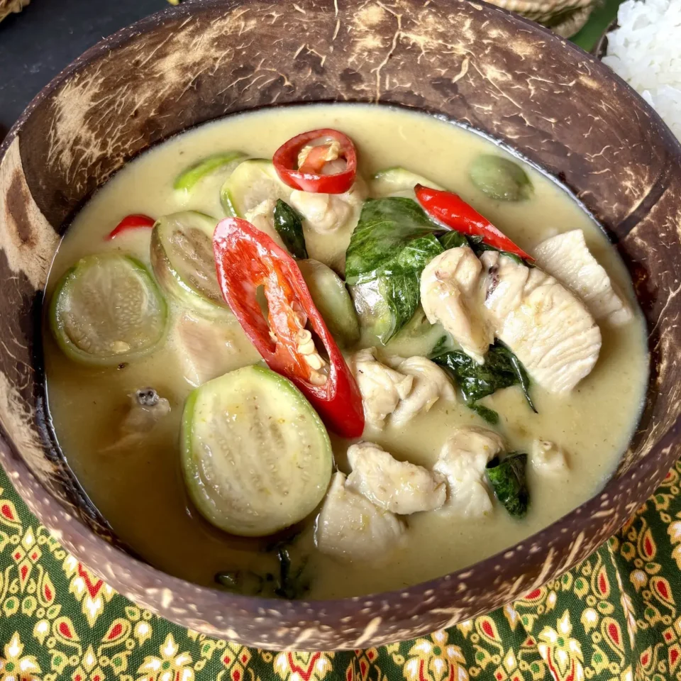Bowl of Thai eggplant green curry with chicken, Thai eggplants, red chili, and Thai basil in a coconut shell bowl.