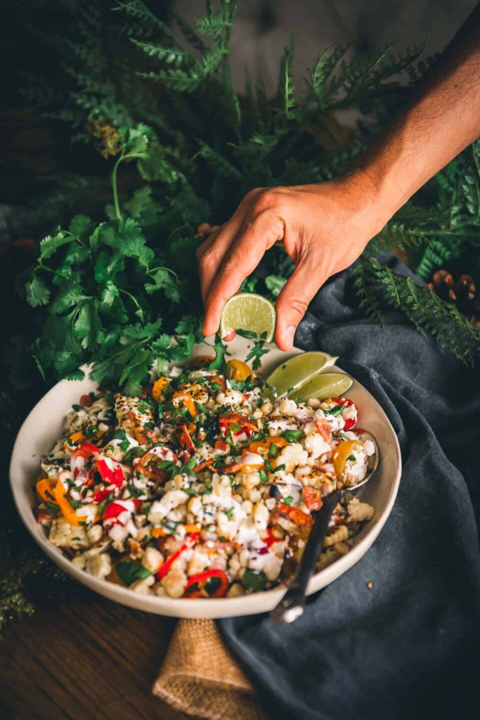 Hand squeezing lime wedge over over salad.