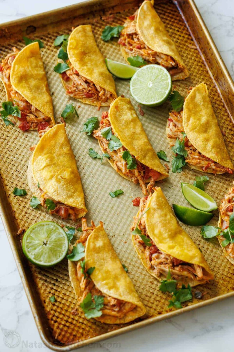 Baked Chicken Tacos on a cooking sheet with lime slices